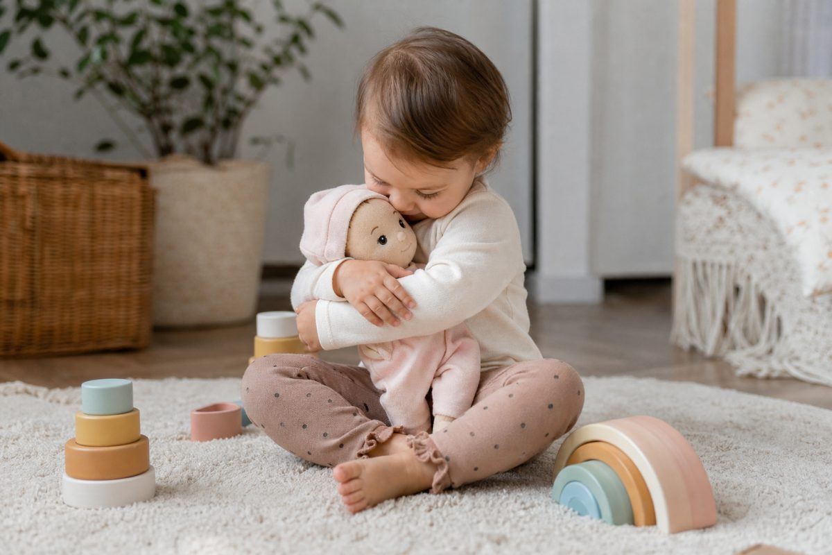 Kisgyerek puha csecsemőbabát ölel a szőnyegen