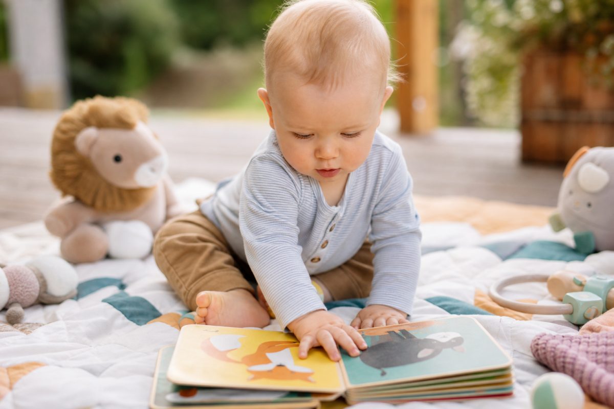 Baba színes lapozó könyvet fog egy játszószőnyegen