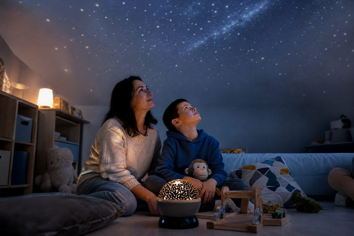 Szülő és gyerek planetárium projektor fényét nézi a szobában